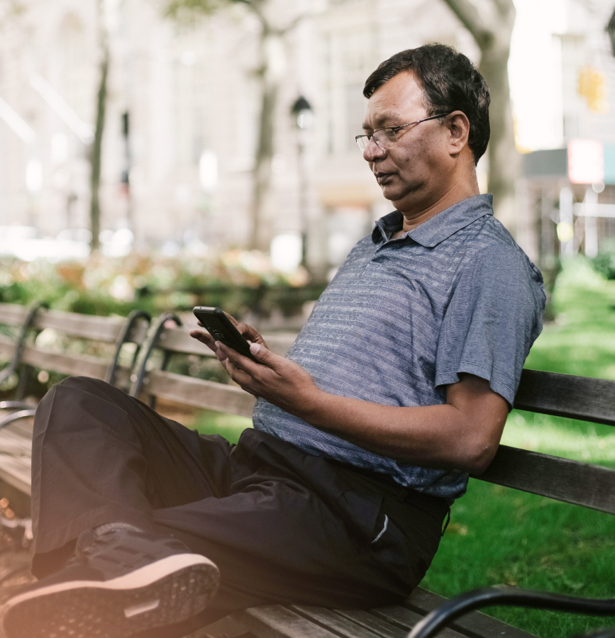 Man in glasses on park bench looking at phone